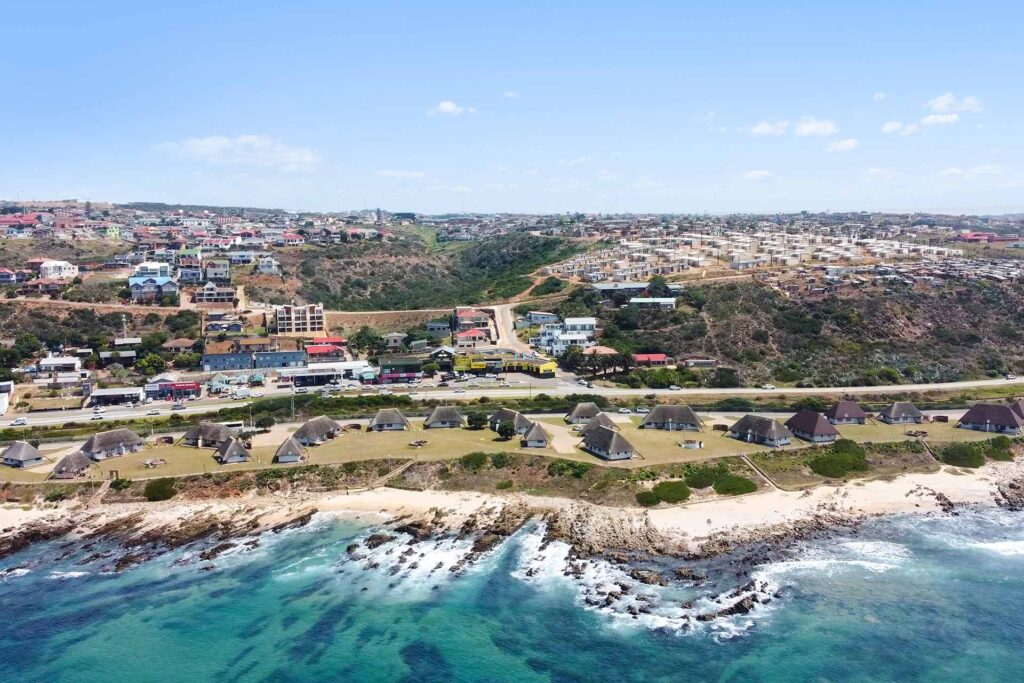 A coastal town with clusters of round, thatched-roof huts near a rocky shoreline and clear turquoise water in the foreground—perfect for exploring De Bakke Santos frequently asked questions about the area’s attractions. @De Bakke Santos Mossel Bay