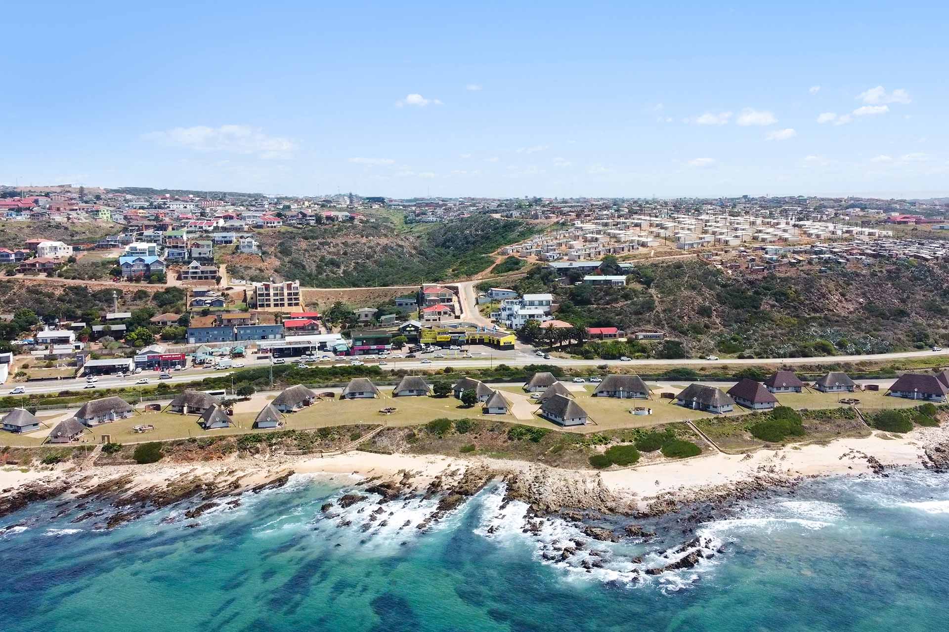 A coastal town with clusters of round, thatched-roof huts near a rocky shoreline and clear turquoise water in the foreground—perfect for exploring De Bakke Santos frequently asked questions about the area’s attractions. @De Bakke Santos Mossel Bay